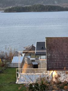 Fotografi av en bygning under utbygging eller renovering, med fokus på en ny terrasse og takkonstruksjon, sett fra en høyde mot et vann.