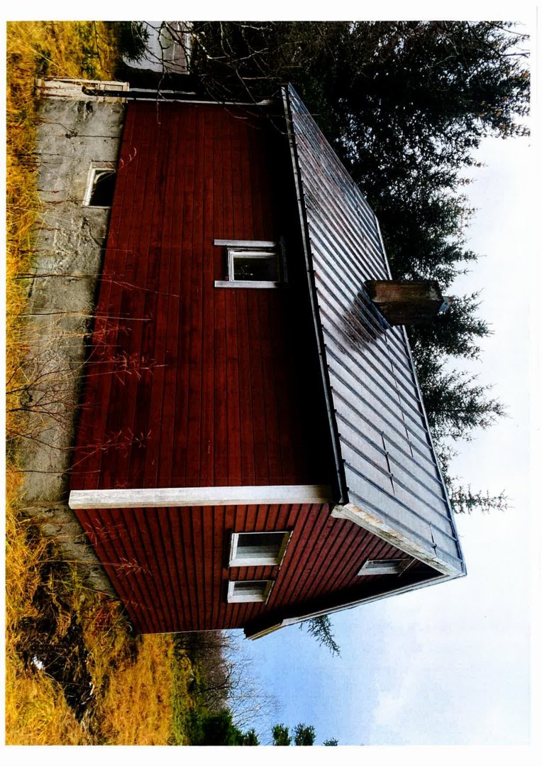 Fotografi av en rød, trepanelt bygning med et skifertak, sett fra en vinkel.