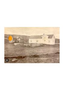 Et gammelt fotografi som viser en hvit bygning og en mørkere bygning i bakgrunnen, sett fra et lavt vinkel.