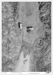 Flyfoto eller satellittbilde av et område med to bygninger og terrengform.