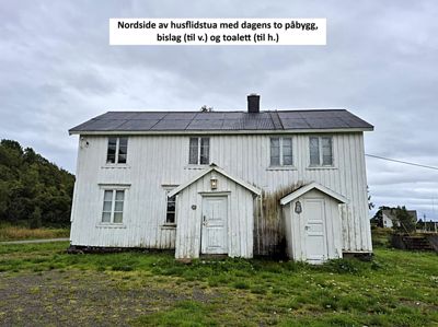 Fotografi av nordfasaden på en hvit, trepanelhus med to påbygg, bislag og toalett.