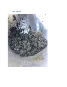 Fotografi av en metallisk beholder som inneholder en mørk, kornet masse, sannsynligvis jordprøve eller en blanding av materialer.