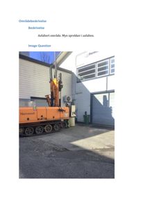 Fotografi av en bygning med en gullfarget boremaskin (Norconsult) parkert foran. Bildet viser et asfaltert område med sprekker.