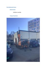 Fotografi av et asfaltert område med en bygning i bakgrunnen og en byggegraver i forgrunnen.