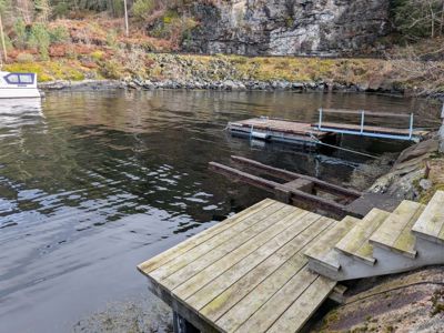 Fotografi av en kai og brygge ved vannkanten med en båt i bakgrunnen.