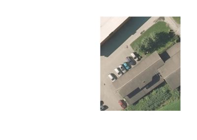 Flyfoto eller satellittbilde av en bygning sett fra oven, med parkerte biler og omgivende beplantning.