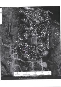 Flyfoto eller satellittbilde av et område med bygninger, veier og natur, med en markert tomt (lilla sirkel) og kartverktøy nederst.