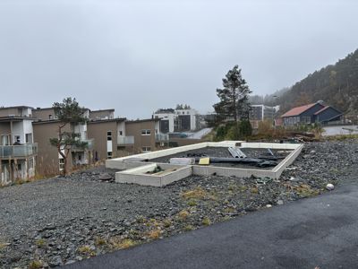 Fotografi av en byggeplass med en ny grunnmur (fundament) i forgrunnen og eksisterende boliger i bakgrunnen.