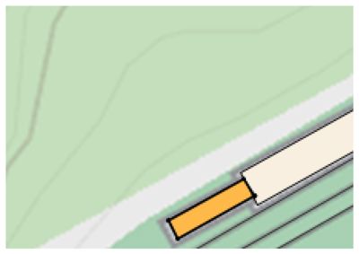 Situasjonsplan som viser en bygning (beige) og en tilhørende struktur (gult) plassert langs en vei eller vei-tilgang, med terrengkonturer i bakgrunnen.