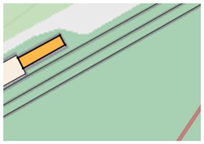 Dette bildet viser en detalj fra en situasjonsplan eller tomtetegning. Det er synlig en bygning (gult og hvitt) plassert i forhold til ei vei (de to parallelle linjene).