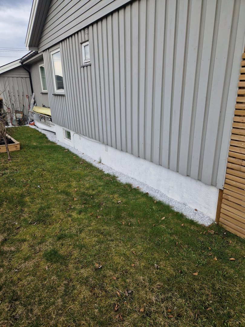 Fotografi av en bygning sett fra siden, som viser fasaden, vinduer, fundament og tilstøtende hage.