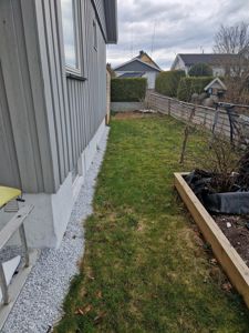 Fotografi av en bygning sett fra siden, med fokus på fasaden, grunnmur og tilstøtende hageområde.