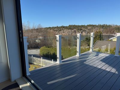 Fotografi av en terrasse med glasshekk og utsikt over vann og kystlandskap.