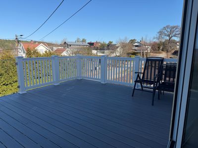 Fotografi av en terrasse med hvit balustrade og mørke møbler, sett fra innendørs mot utsiden.