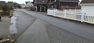 Fotografi av en vei i et boligområde med hus, hekk og parkeringsplasser.