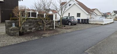 Fotografi av en eksisterende eller ferdigstilt bolig med fortau, hekk, bil og søppelcontainere.