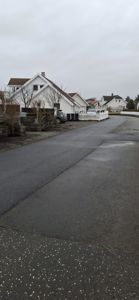 Fotografi av en boligbebyggelse med vei, hager og parkeringsplasser.