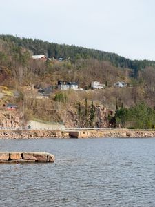 Fotografi av et kystlandskap med hus på en skråning og vann i forgrunnen.