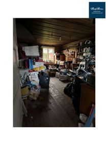 Fotografi av et innendørs rom, sannsynligvis en garasje eller lager, som er fullt av gjenstander og ser ut til å være i dårlig stand.