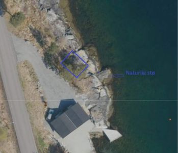 Flyfoto eller satellittbilde av et kystområde med en markert tomt (blå linje) og en vei. Bildet inneholder også en tekstmerking 'Naturlig stø' med en pil.