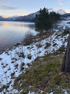 Fotografi av en bygning ved en vannflate med fjell i bakgrunnen.