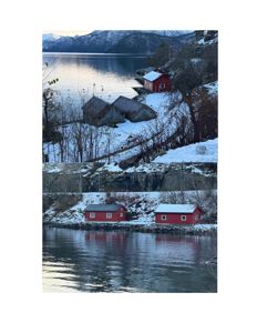 Fotografi av en bygning (eller flere småbygninger) ved vannet i et vinterlandskap.