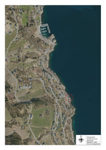 Flyfoto som viser et område langs en kystlinje med en markert bygning (rødt rektangel) og en kompassrose.