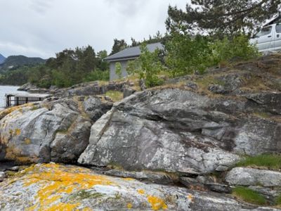 Fotografi av en bygning plassert på en steinete kystlinje med vann i bakgrunnen.