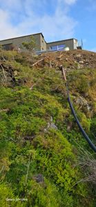 Fotografi av en bygning plassert på en bratt, vegetasjonstett skråning. Bildet viser terrenget og bygningens plassering i forhold til naturen.