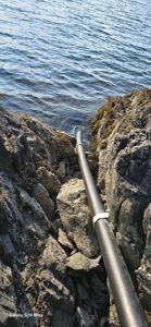 Fotografi av en svart rørledning som løper langs en steinete kystlinje ut til vannet.