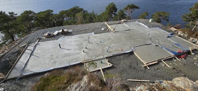 Fotografi av en byggeplass som viser en nybetont betongplate (sannsynligvis grunnplaten) med formstaver og armeringsstenger på en kysttomt.