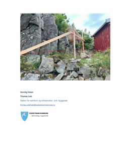 Fotografi av en steinmur med et trekonstruksjon (troll) og en rød bygning i bakgrunnen.