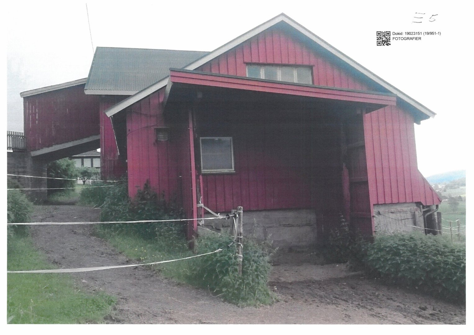 Fotografi av en rød, langhusliknende bygning (muligens en uthus eller garasje) sett fra siden.