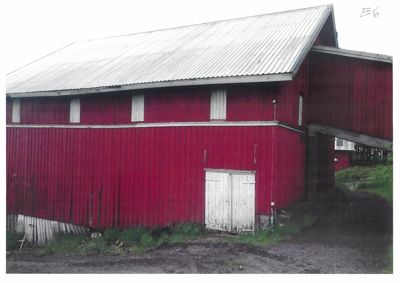 Fotografi av en rød, toetasjes bygning (sannsynligvis en uthus eller skur) med hvit takbelegg og hvite dører/vinduer.