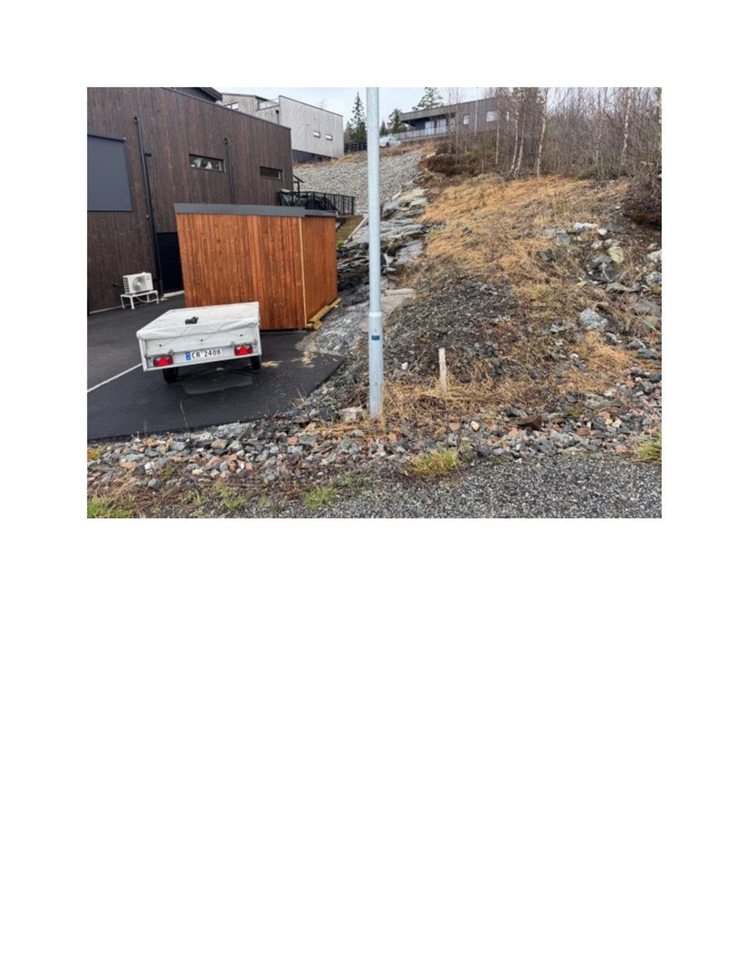 Fotografi av en bygning med mørk fasade og en mindre uthus, sett fra bakkenivå med en bakke i forgrunnen.