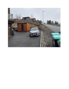 Fotografi av en bygning (kanskje en hytte eller container) på en tomt med bil og søppelcontainere i forgrunnen.