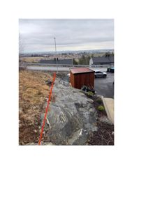 Fotografi av et utsnitt av en tomt med stein, en liten uthus, og utsikt over nabolag.