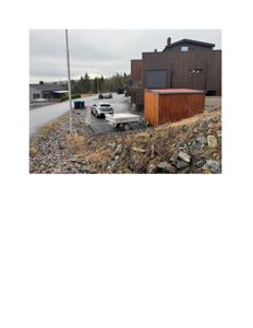 Fotografi av en moderne bygning med mørk fasade og en mindre utedekkning, sett fra en skråning.