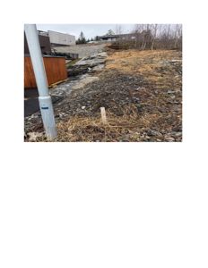 Fotografi av et utendørs område med en bygning i bakgrunnen, en grusvei og en markørstang i forgrunnen.