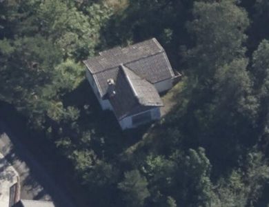 Flyfoto eller satellittbilde av en bygning sett fra luften, omgitt av skog.