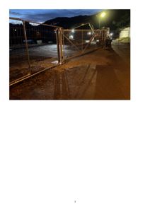 Fotografi av en byggeplass eller anleggsområde om natten, med en stengselport i forgrunnen og en graver i bakgrunnen.