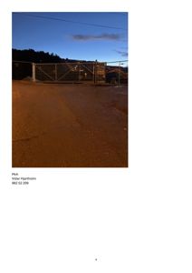 Fotografi av en gate eller inngangsparti med en metallgjerdeport, en grøft og en bygning i bakgrunnen mot kveldshimmel.