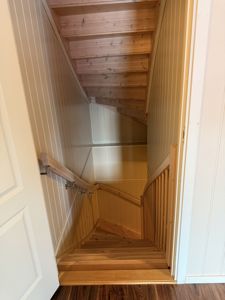 Fotografi av en trapp med tretrinn og håndtak, sett fra inngangen nedover.