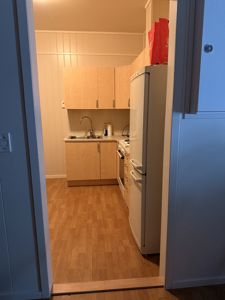 Fotografi av en kjøkkenrom med lyse skap, hvit kjøleskap og gulvpanel.