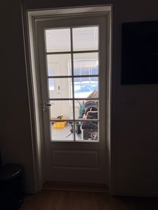 Fotografi av en hvit dør med glassfelt sett innad i en bolig. Døren leder ut til en terrasse eller hage der det er snø på bakken.