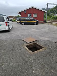 Fotografi av en rød bygning (muligens en stasjon eller uthus) sett fra bakkenivå, med bil og jernbanespor i nærheten.