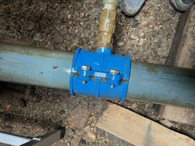 Fotografi av en blå ventil eller kobling på en stor vann- eller avløpsrør i graven.