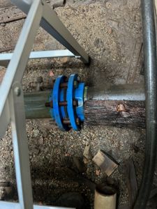 Fotografi av en rørledning med en blå flenskobling (flange) i grus under bakken.