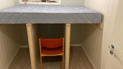 Fotografi av en innredet soverom med en sengeramme (høyseng) og en oransje stol under.