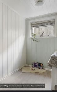 Fotografi av et innendørs rom (kanskje kontor eller soverom) med hvite panelvegger, gulv og et vindu.